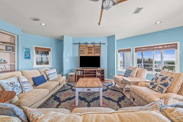 living room with a barn door, ceiling fan, and built in shelves