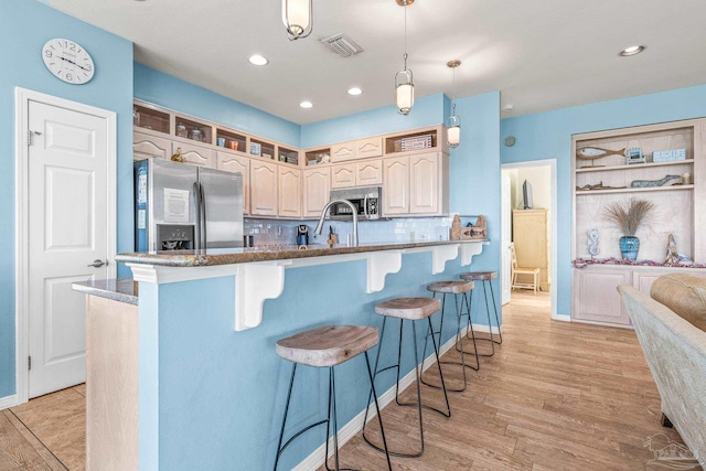 kitchen featuring a breakfast bar area, decorative backsplash, hanging light fixtures, light hardwood / wood-style floors, and stainless steel appliances