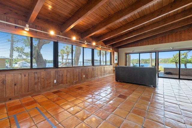 unfurnished living room with vaulted ceiling with beams, wood walls, a water view, wooden ceiling, and light tile patterned floors