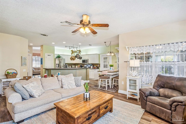 living room with ceiling fan, light hardwood / wood-style floors, a textured ceiling, and a wealth of natural light