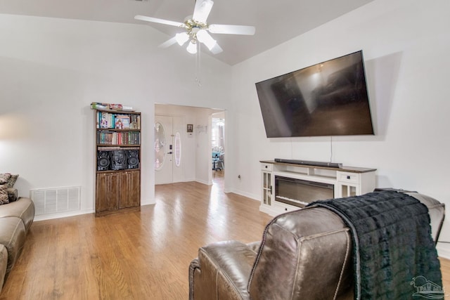 living area with light wood-style floors, ceiling fan, baseboards, visible vents, and high vaulted ceiling