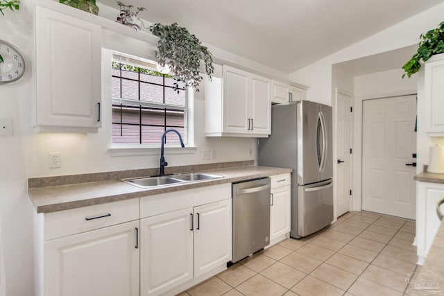kitchen with a sink, light tile patterned floors, vaulted ceiling, white cabinets, and appliances with stainless steel finishes