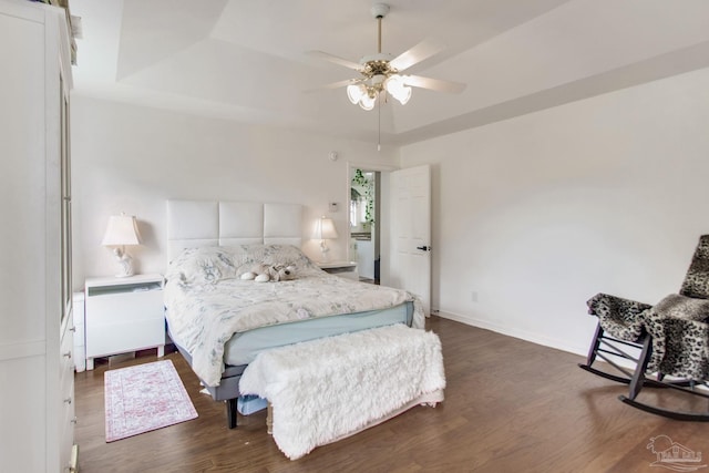 bedroom with a ceiling fan, a tray ceiling, dark wood finished floors, and baseboards