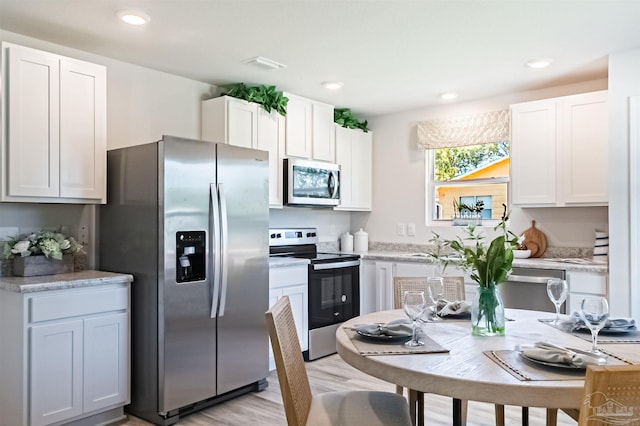 kitchen with white cabinets, light wood-type flooring, and appliances with stainless steel finishes