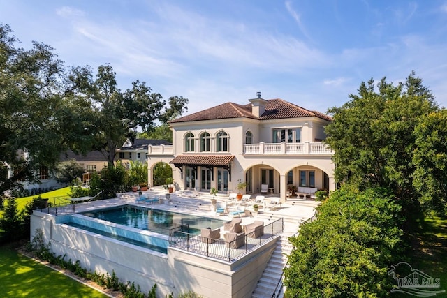 rear view of property featuring a swimming pool with hot tub, a balcony, and a patio