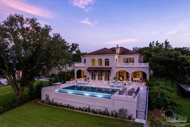 back house at dusk with a patio area, a balcony, a fenced in pool, and a yard