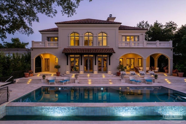 back house at dusk with a patio area, a balcony, and french doors