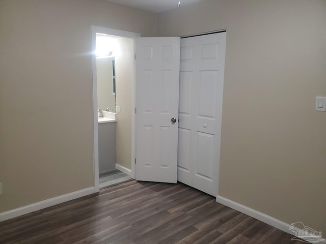 unfurnished bedroom featuring ensuite bathroom, dark wood-style flooring, a closet, and baseboards