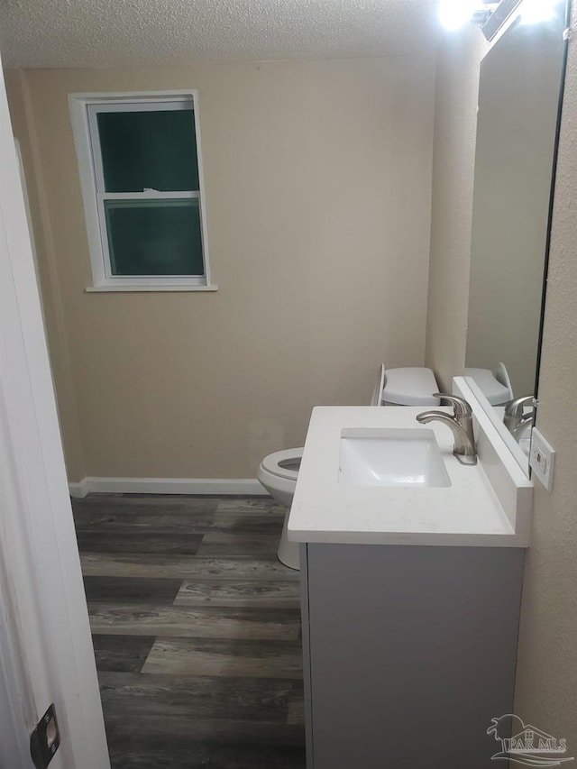 bathroom with a textured ceiling, toilet, wood finished floors, vanity, and baseboards