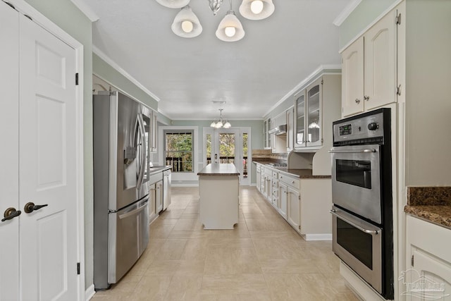 kitchen featuring appliances with stainless steel finishes, white cabinetry, ornamental molding, a center island, and an inviting chandelier