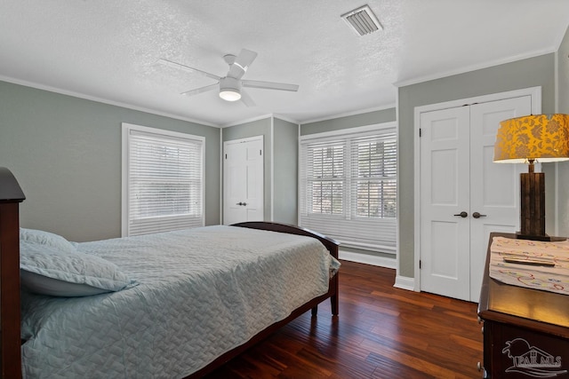 bedroom featuring crown molding, ceiling fan, a textured ceiling, dark hardwood / wood-style flooring, and multiple closets