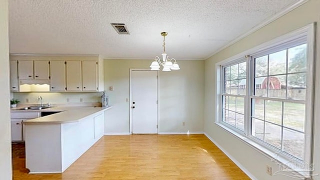 kitchen with pendant lighting, sink, light hardwood / wood-style floors, kitchen peninsula, and an inviting chandelier