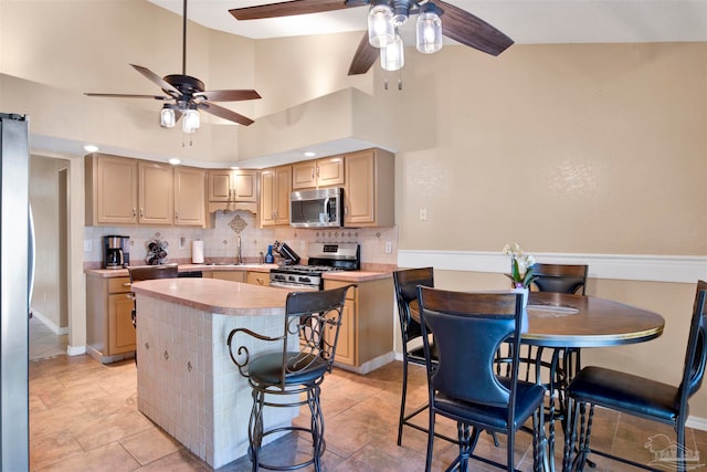 kitchen featuring tasteful backsplash, a kitchen island, appliances with stainless steel finishes, high vaulted ceiling, and a kitchen bar