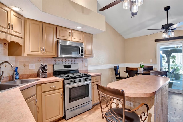 kitchen with light brown cabinets, stainless steel appliances, sink, vaulted ceiling, and ceiling fan