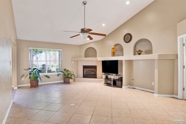 unfurnished living room with ceiling fan, high vaulted ceiling, a tiled fireplace, and light tile patterned floors