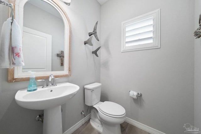 half bath featuring wood finished floors, toilet, and baseboards
