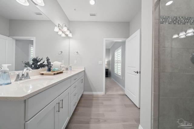 bathroom with a sink, double vanity, visible vents, baseboards, and wood finished floors