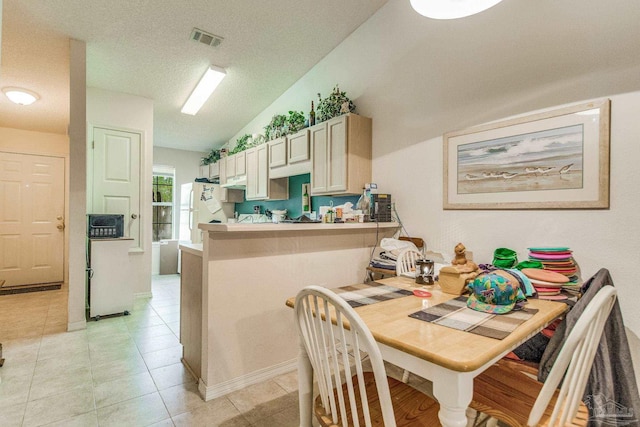 kitchen with a textured ceiling, white fridge, light tile patterned floors, kitchen peninsula, and lofted ceiling