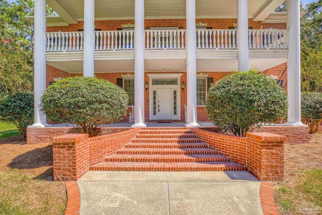 entrance to property with covered porch, brick siding, and a balcony