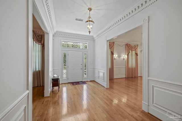 entryway featuring light wood finished floors, visible vents, a decorative wall, crown molding, and a wainscoted wall