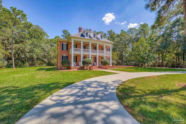 greek revival house with a chimney, a front yard, brick siding, and covered porch