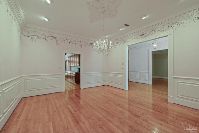 unfurnished dining area featuring a decorative wall, an inviting chandelier, crown molding, and light wood-style flooring