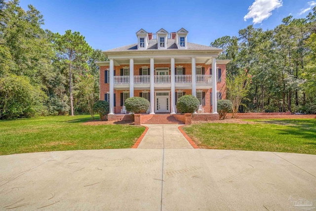 greek revival house featuring covered porch, a front yard, brick siding, and a balcony