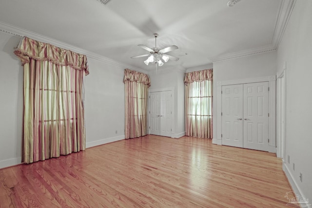 unfurnished bedroom featuring crown molding, two closets, and light wood-style flooring