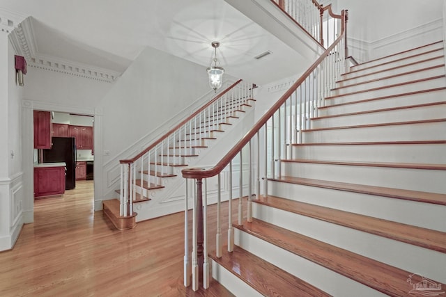 stairs with visible vents, a chandelier, a decorative wall, a towering ceiling, and wood finished floors