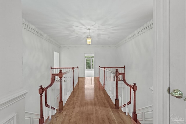 corridor featuring an upstairs landing, a decorative wall, crown molding, and wood finished floors