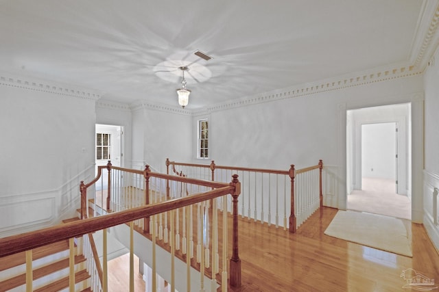 corridor featuring crown molding, wood finished floors, visible vents, and an upstairs landing