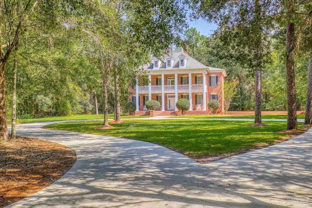 greek revival house with a front lawn, a porch, driveway, and a balcony