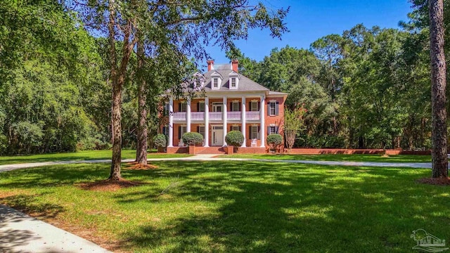 greek revival house featuring a porch, a front lawn, a chimney, and a balcony