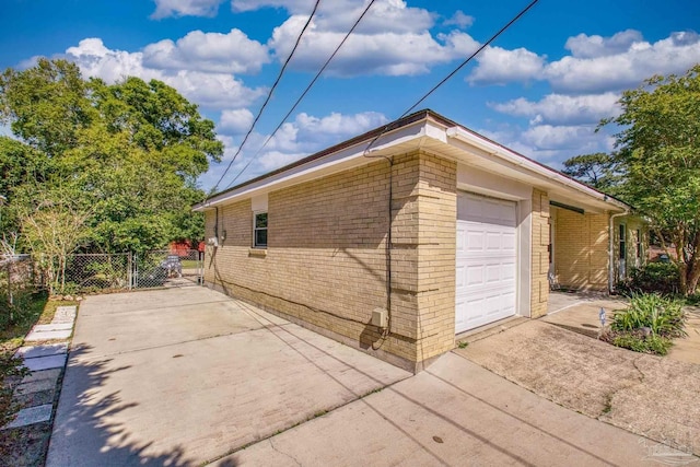 view of home's exterior with an attached garage, fence, brick siding, a gate, and driveway