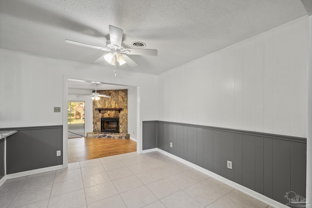 unfurnished living room with a fireplace, light tile patterned floors, a textured ceiling, wainscoting, and ceiling fan