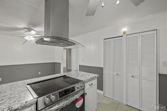 kitchen with ceiling fan, stainless steel electric stove, a textured ceiling, wainscoting, and island range hood