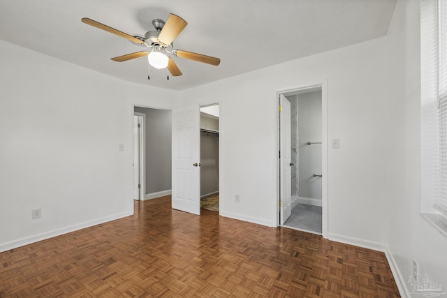 unfurnished bedroom with a spacious closet, ensuite bathroom, baseboards, and a ceiling fan