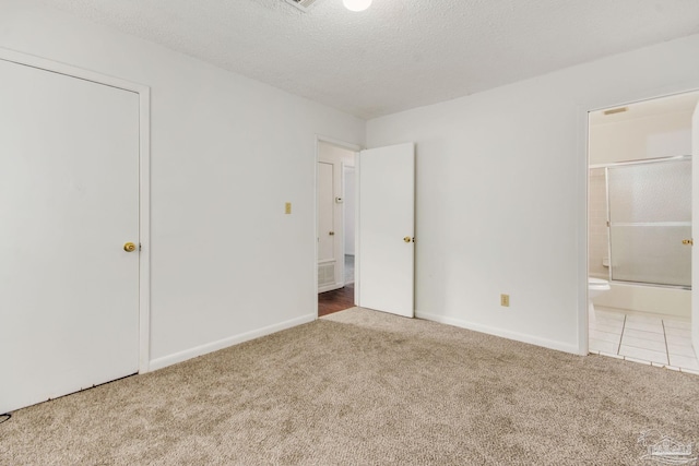 unfurnished bedroom featuring carpet flooring, ensuite bathroom, and a textured ceiling