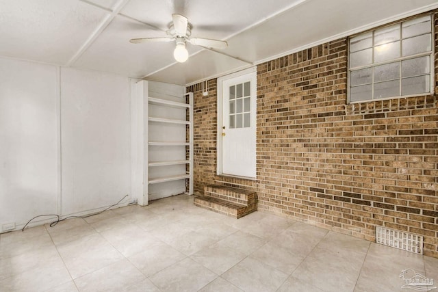 unfurnished room featuring built in shelves, ceiling fan, and brick wall