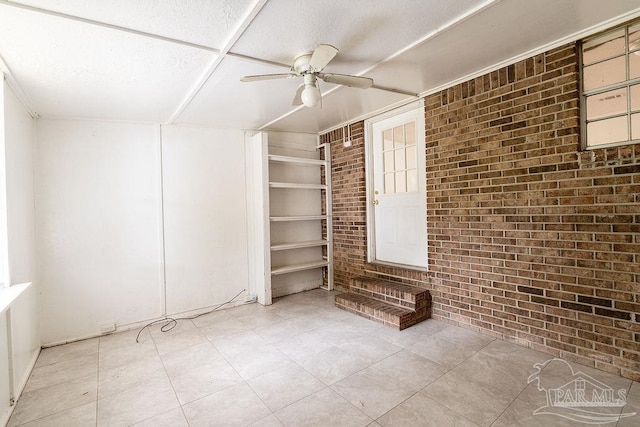 spare room with ceiling fan and brick wall