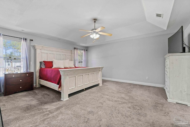 carpeted bedroom with ceiling fan and a raised ceiling