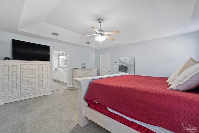 carpeted bedroom featuring a tray ceiling, ensuite bath, and ceiling fan