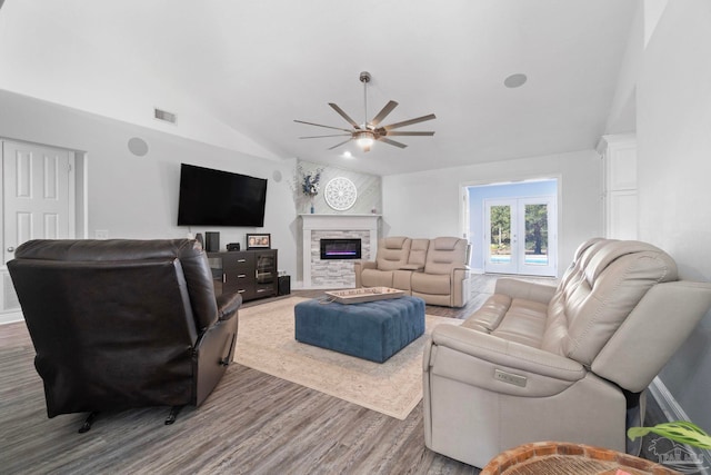 living room with french doors, vaulted ceiling, ceiling fan, hardwood / wood-style flooring, and a stone fireplace