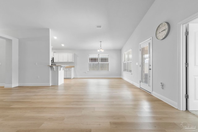 unfurnished living room featuring an inviting chandelier, light hardwood / wood-style flooring, and lofted ceiling