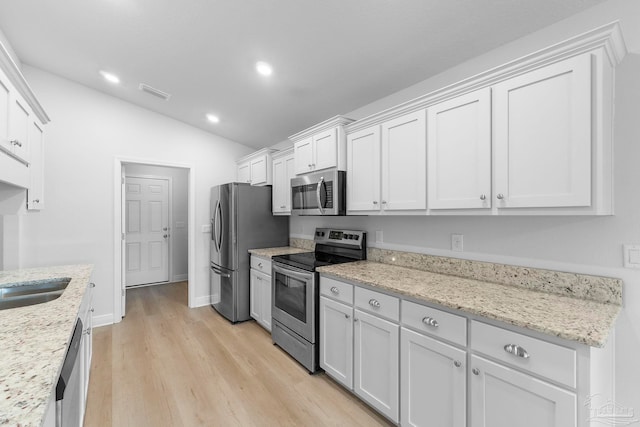 kitchen featuring white cabinetry, vaulted ceiling, stainless steel appliances, and light hardwood / wood-style flooring