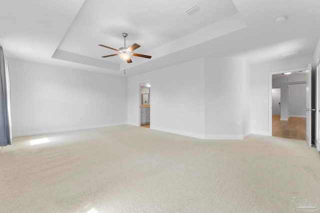 spare room with ceiling fan, a tray ceiling, and light colored carpet