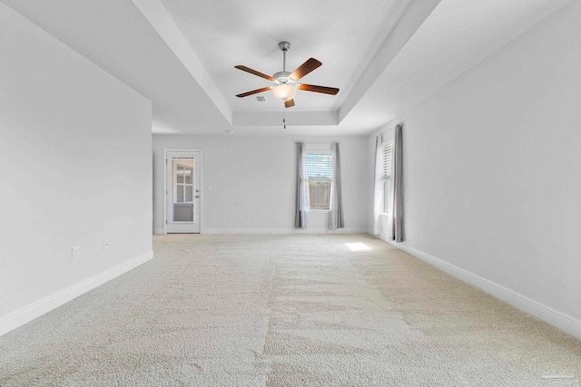 empty room with ceiling fan, carpet floors, and a tray ceiling