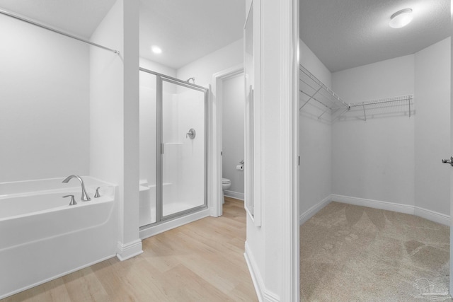 bathroom with a textured ceiling, shower with separate bathtub, hardwood / wood-style floors, and toilet