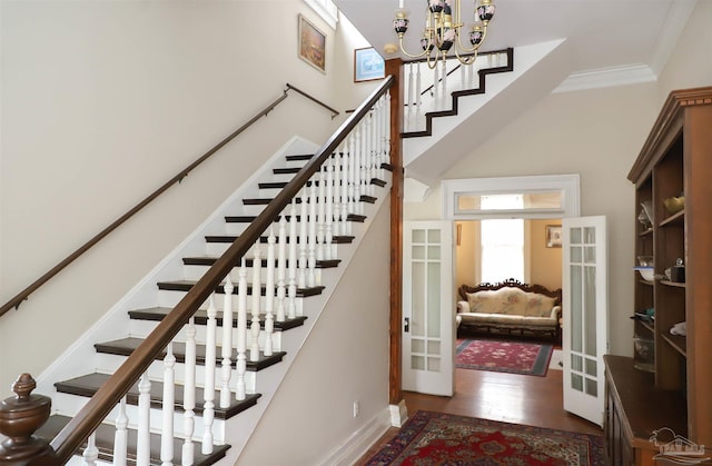 stairs with french doors, ornamental molding, wood-type flooring, and an inviting chandelier