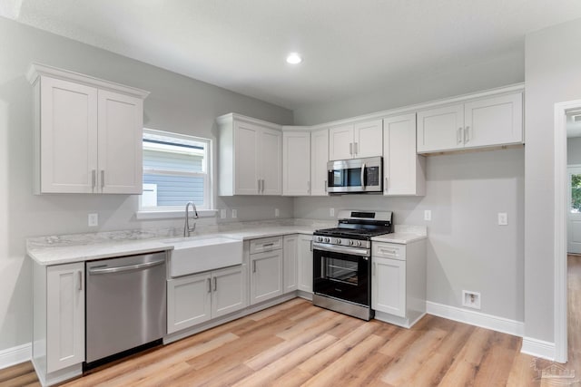 kitchen with baseboards, a sink, appliances with stainless steel finishes, white cabinetry, and light wood-type flooring